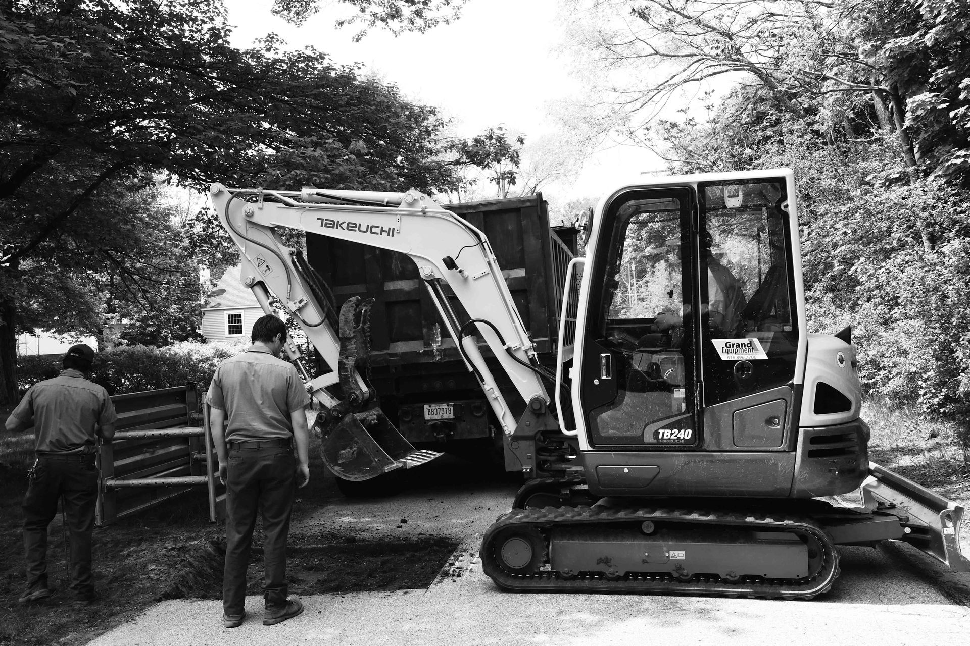 Two men standing near an excavator loading a dump truck in a wooded area.