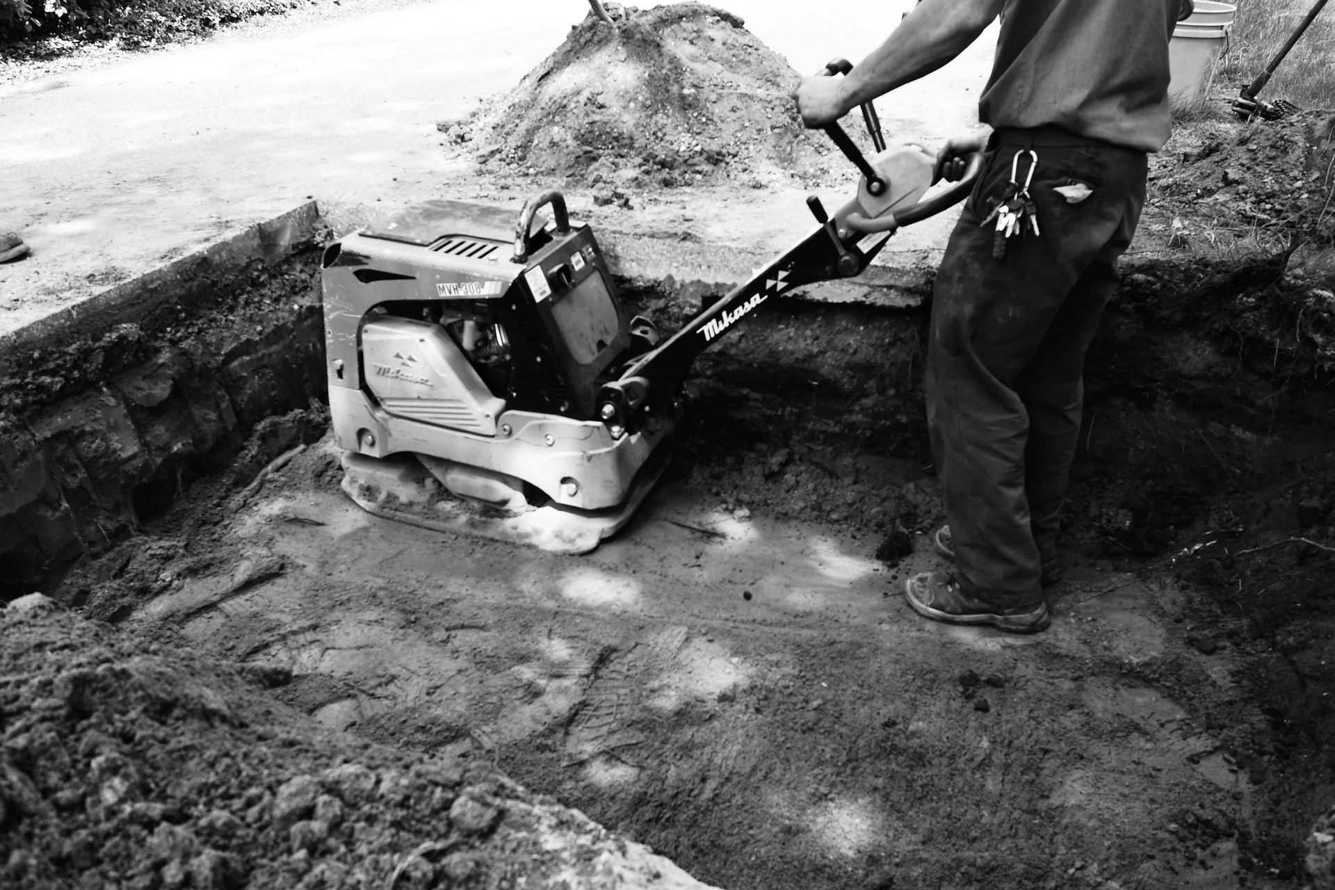 Man using a plate compactor on soil in a construction site.