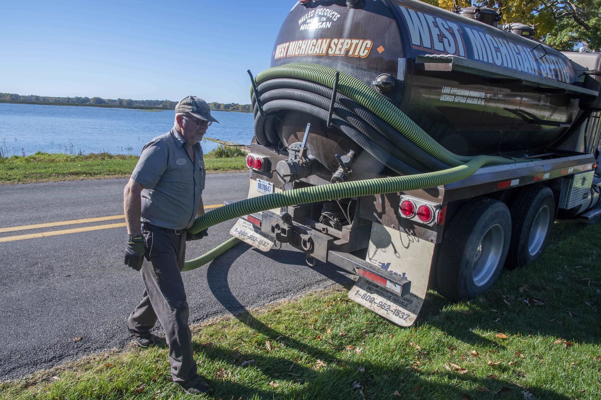 Man in uniform pulls hose from septic tank truck near water.