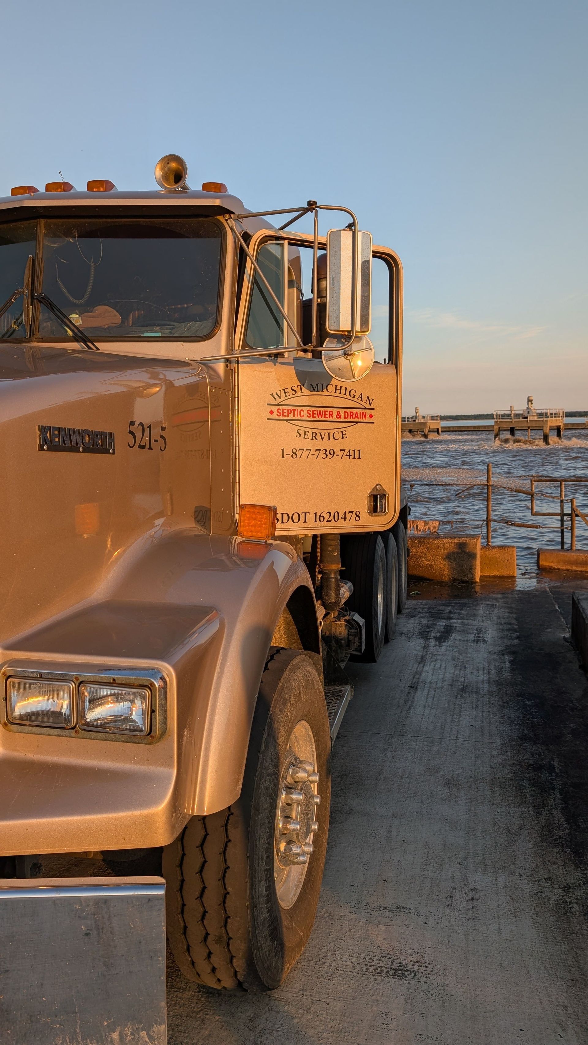 Brown semi-truck parked on a dark road next to a body of water at sunset.