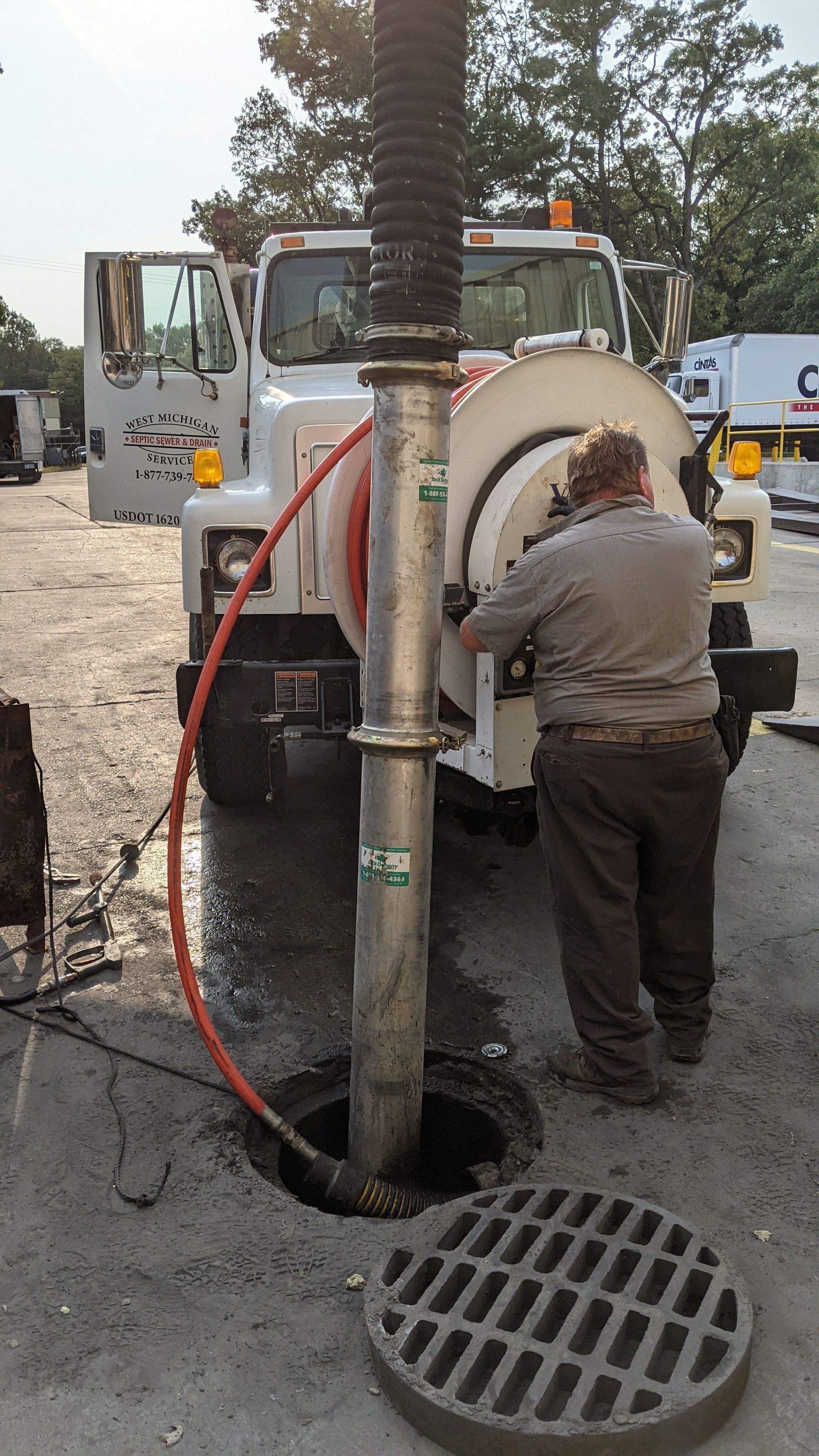 Man using a truck-mounted sewer cleaner on a street. Grey concrete, black sewer, grey truck.