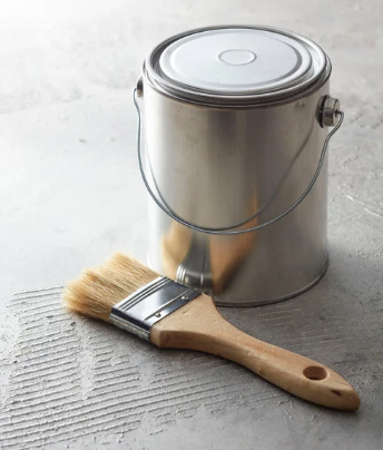 Paint can with closed lid and paintbrush resting on a textured gray surface.