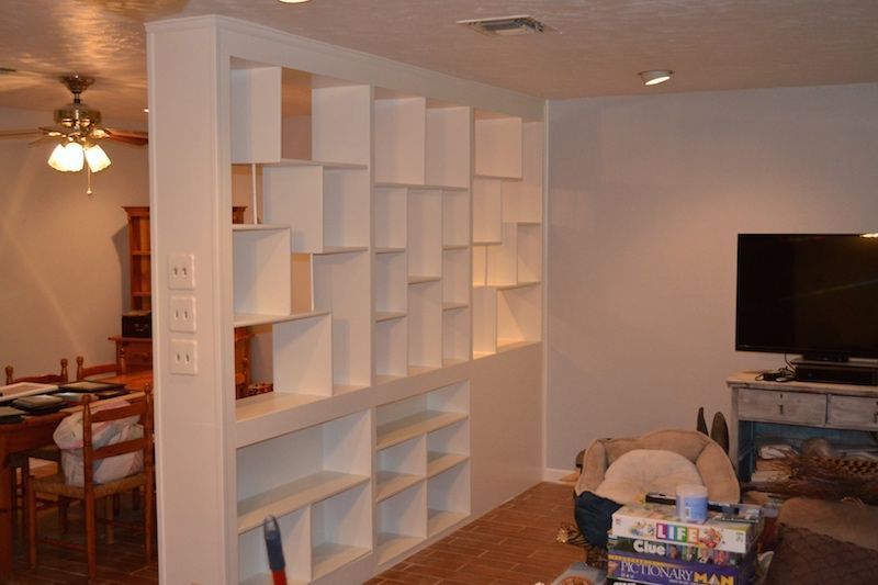 White shelving unit used as a room divider, with a dining area on one side and living area with TV on the other.
