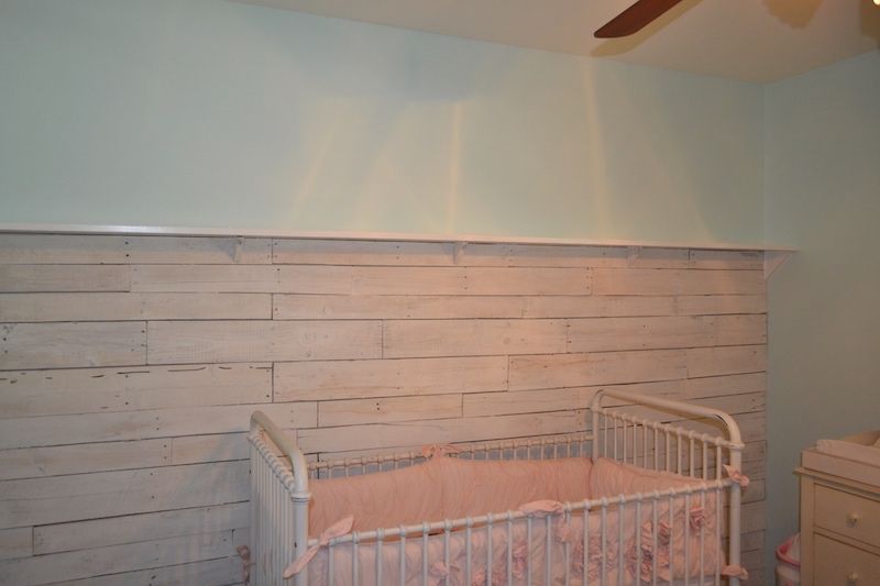 White crib with pink bedding in a room with a distressed white plank accent wall and light blue walls.