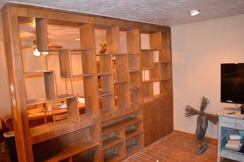 Wooden room divider with open shelves in a room with a TV and decorative items.