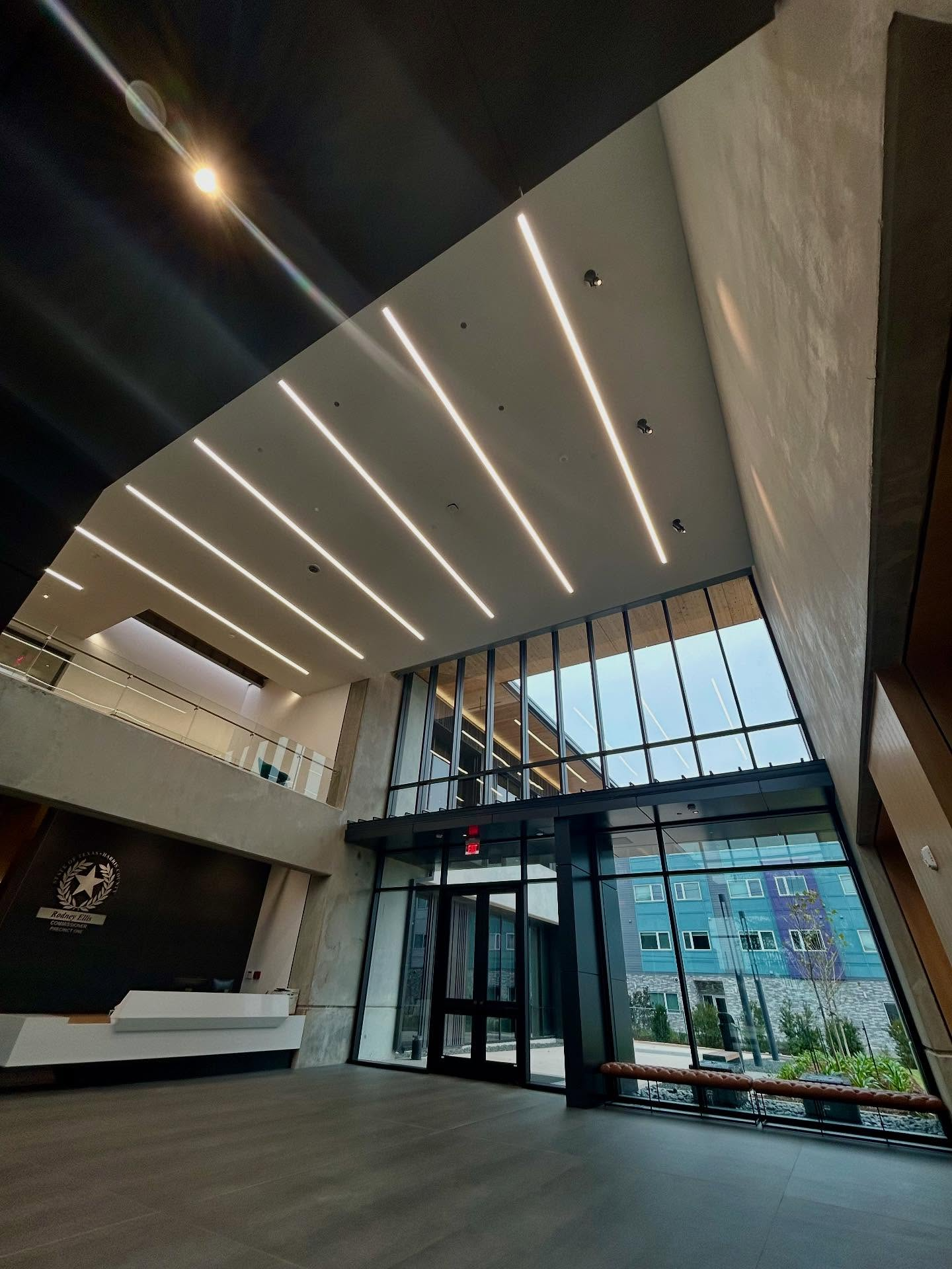 Modern building interior with large windows and linear ceiling lights. Grey and black walls.