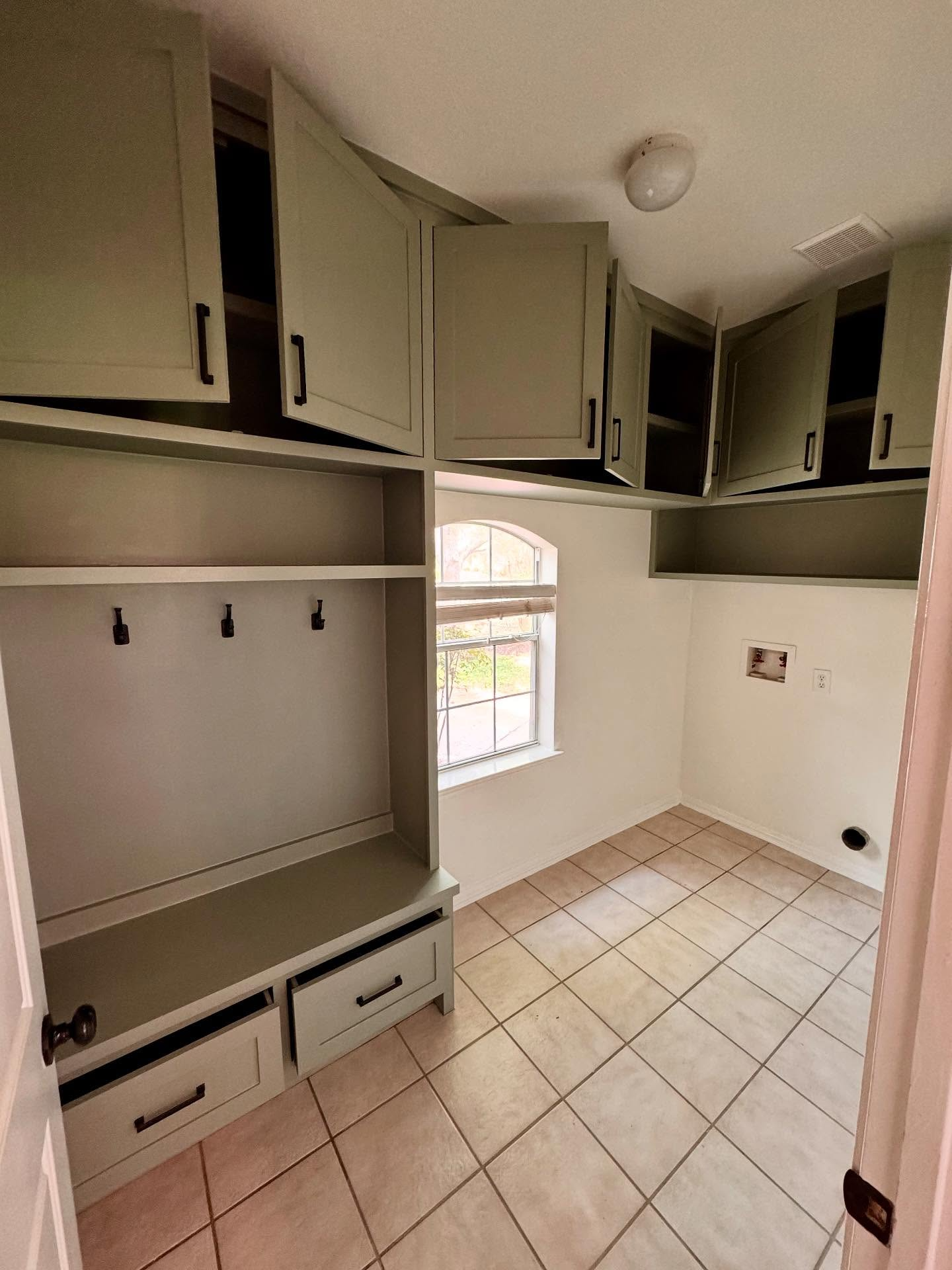 Laundry room with light green cabinets, bench with hooks, drawers, and tile floor.