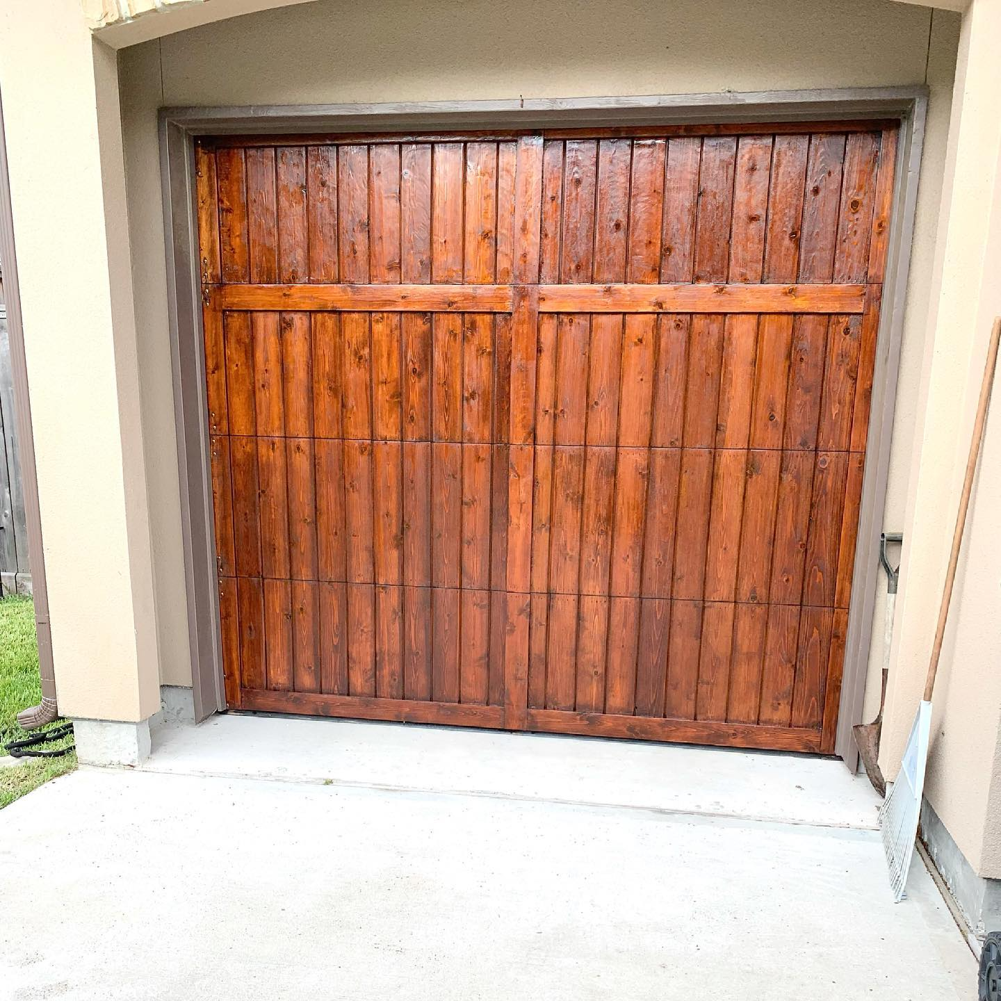 Wooden garage door, brown with vertical planks, concrete driveway, and tan trim.