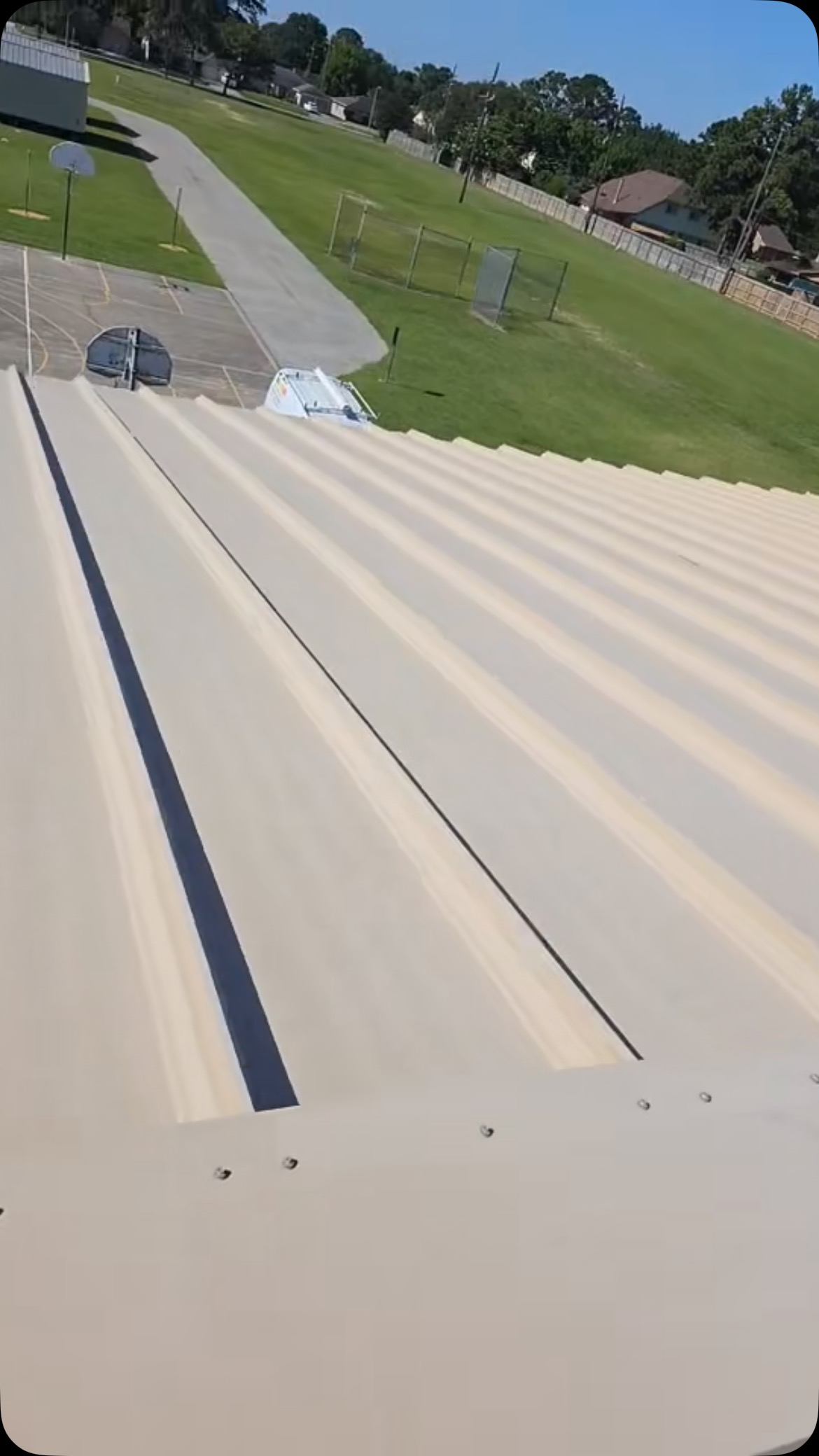 View of a corrugated metal roof with a grassy hill and road in the background under a blue sky.