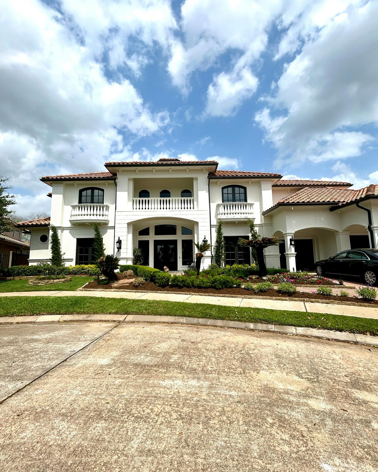 White stucco mansion with red tile roof, arched windows, and manicured lawn under a cloudy sky.