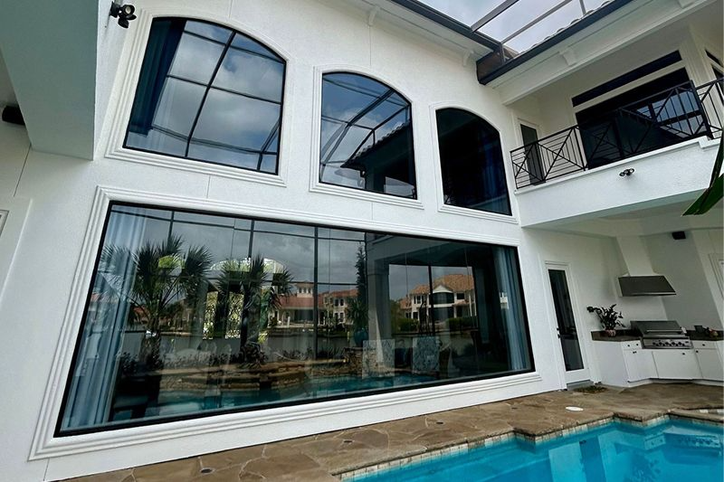 White house exterior with large glass windows overlooking a pool.