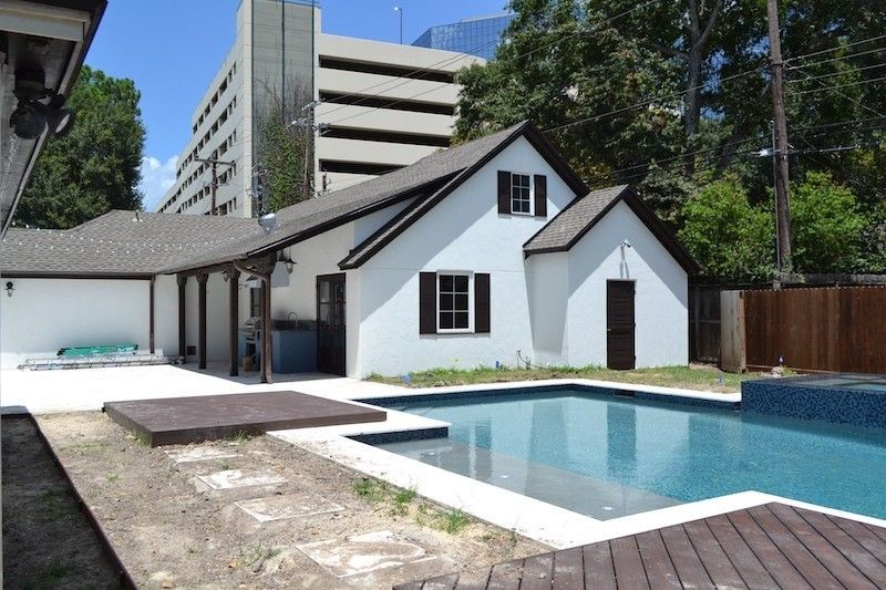 Backyard with a white house, pool, and patio. A parking garage is in the background.