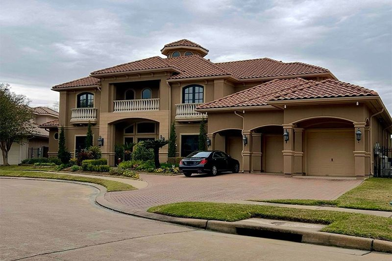 Large tan house with terracotta roof, two-car garage, and black car parked in the driveway.
