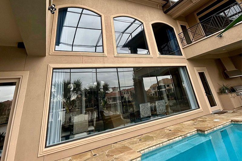 Beige home exterior with large glass windows overlooking a pool.