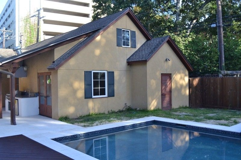 Small tan building with dark shutters and a pool in the foreground.