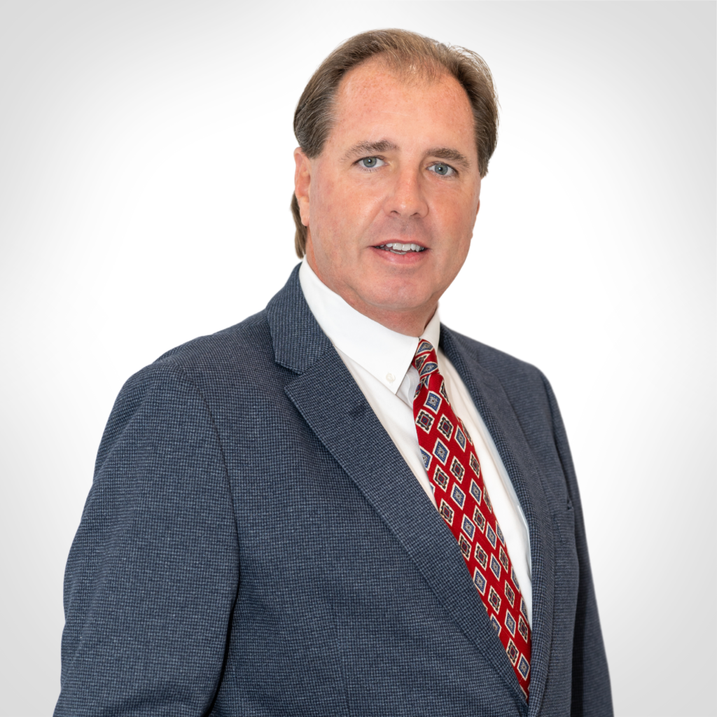 Professional headshot of a man in a dark suit and red patterned tie against a white background