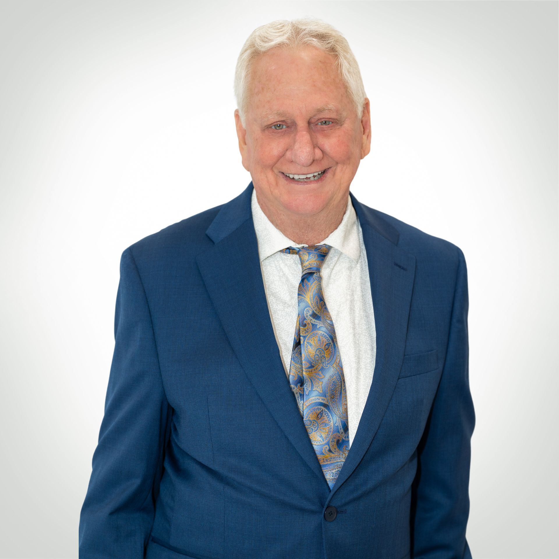 Smiling man in a blue suit with patterned tie, standing against a white background