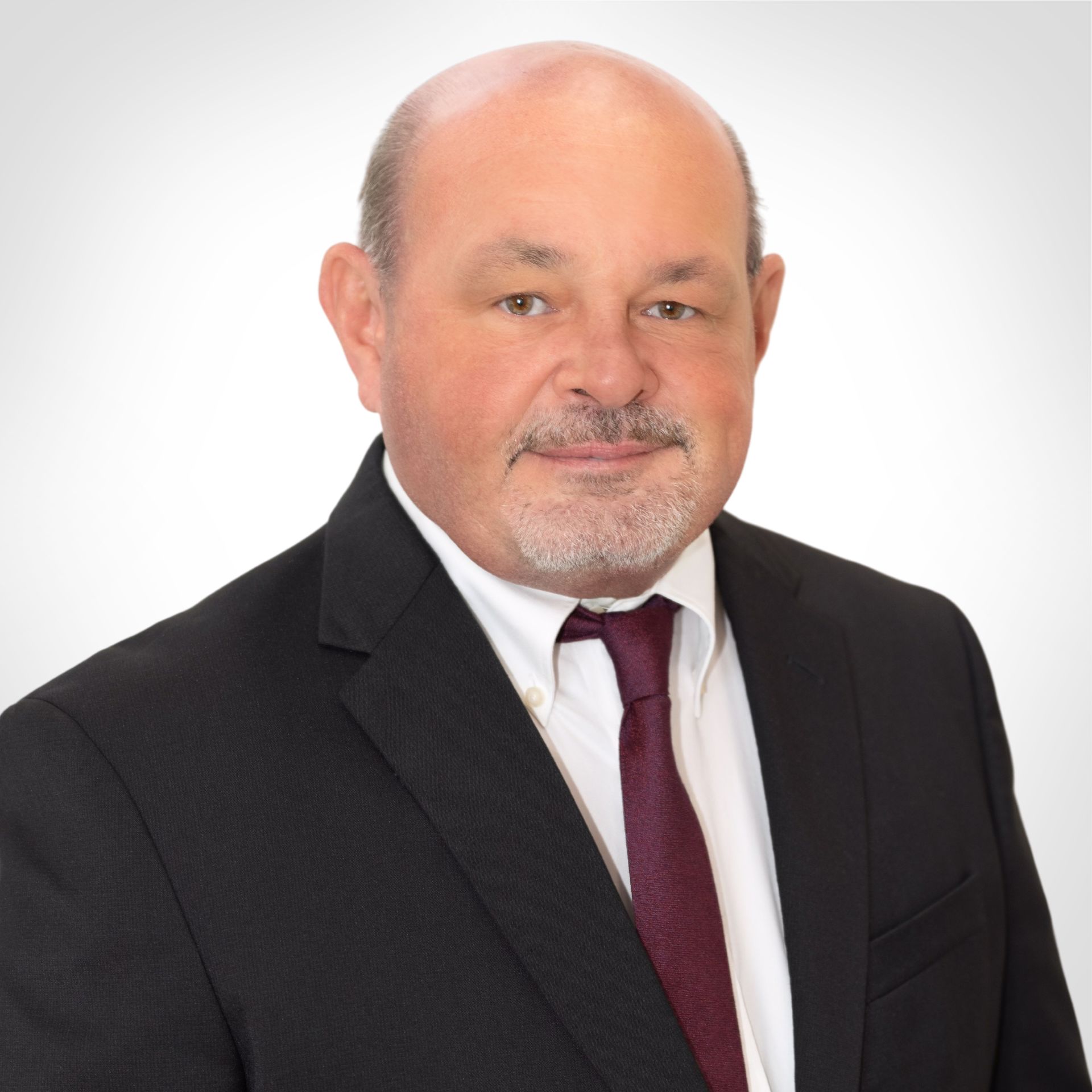 Professional headshot of a man in a dark suit, white shirt, and burgundy tie against a white background