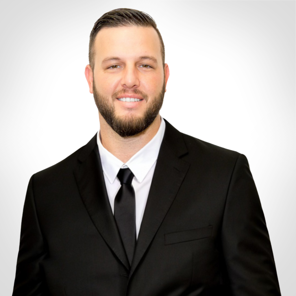 Man in a black suit and tie smiling against a light gray background