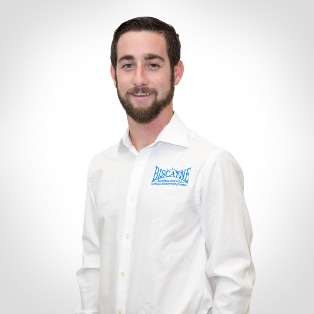 Smiling man in a white dress shirt with a blue logo, standing against a white background