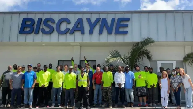 Group of people standing outside a building with a large “BISCAYNE” sign, many wearing bright yellow shirts.