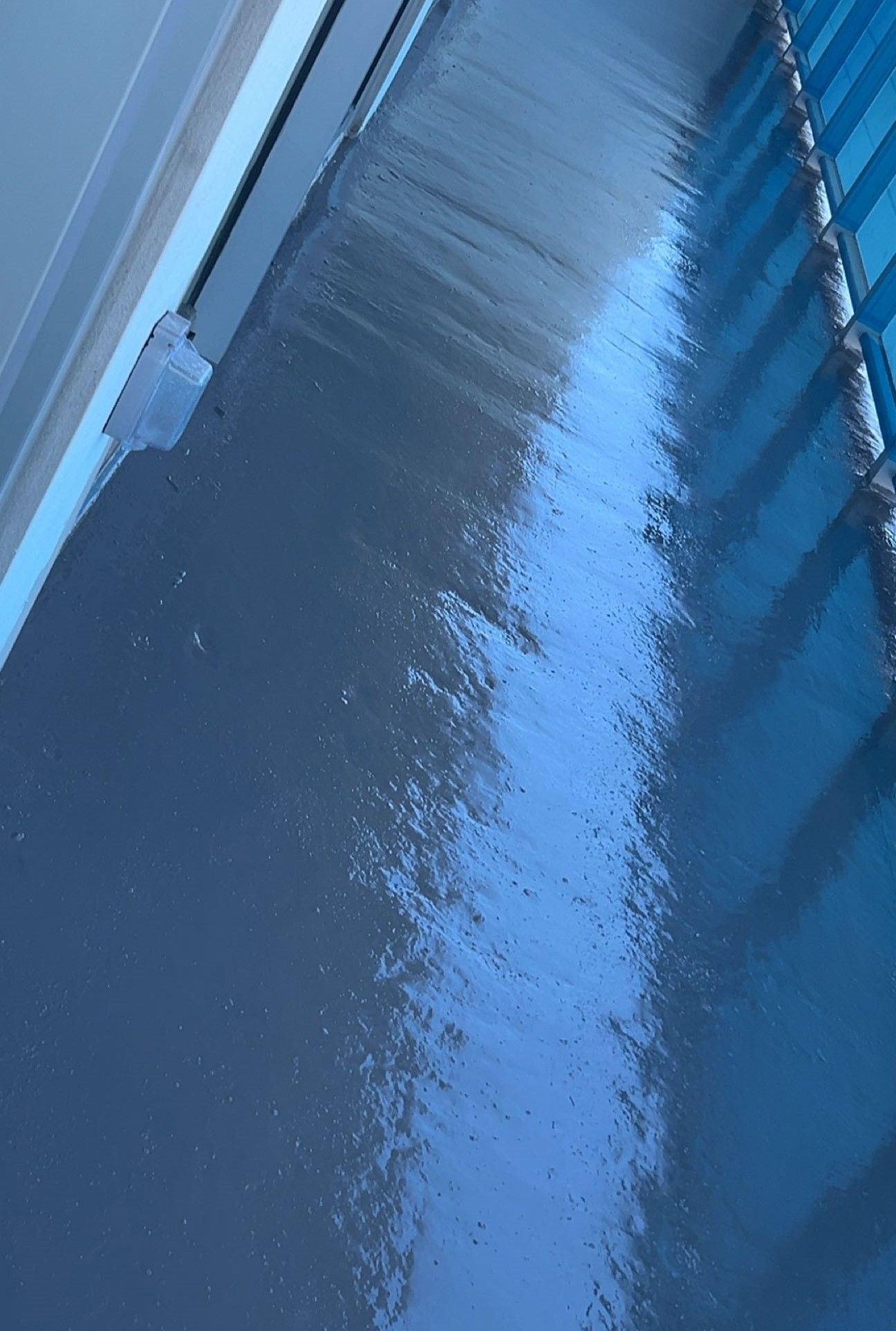 Snow-covered walkway beside a building and metal railing, viewed at an angle.