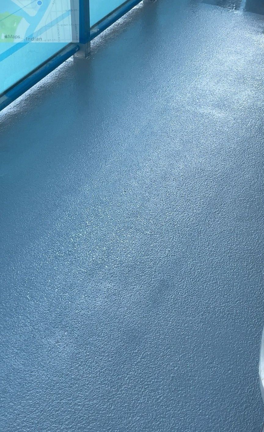 Blue textured pool deck beside a swimming pool with a metal railing along the left side
