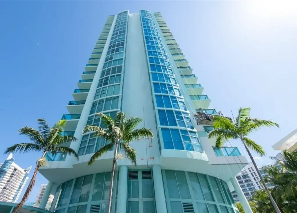 Tall turquoise high-rise building with palm trees against a clear blue sky