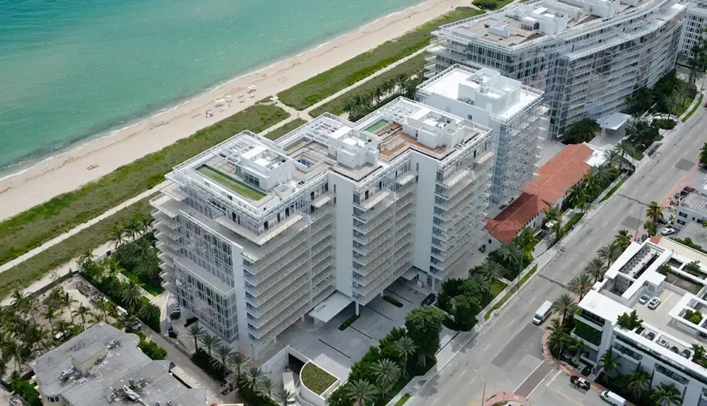 Aerial view of a modern beachfront apartment complex beside a road and turquoise sea