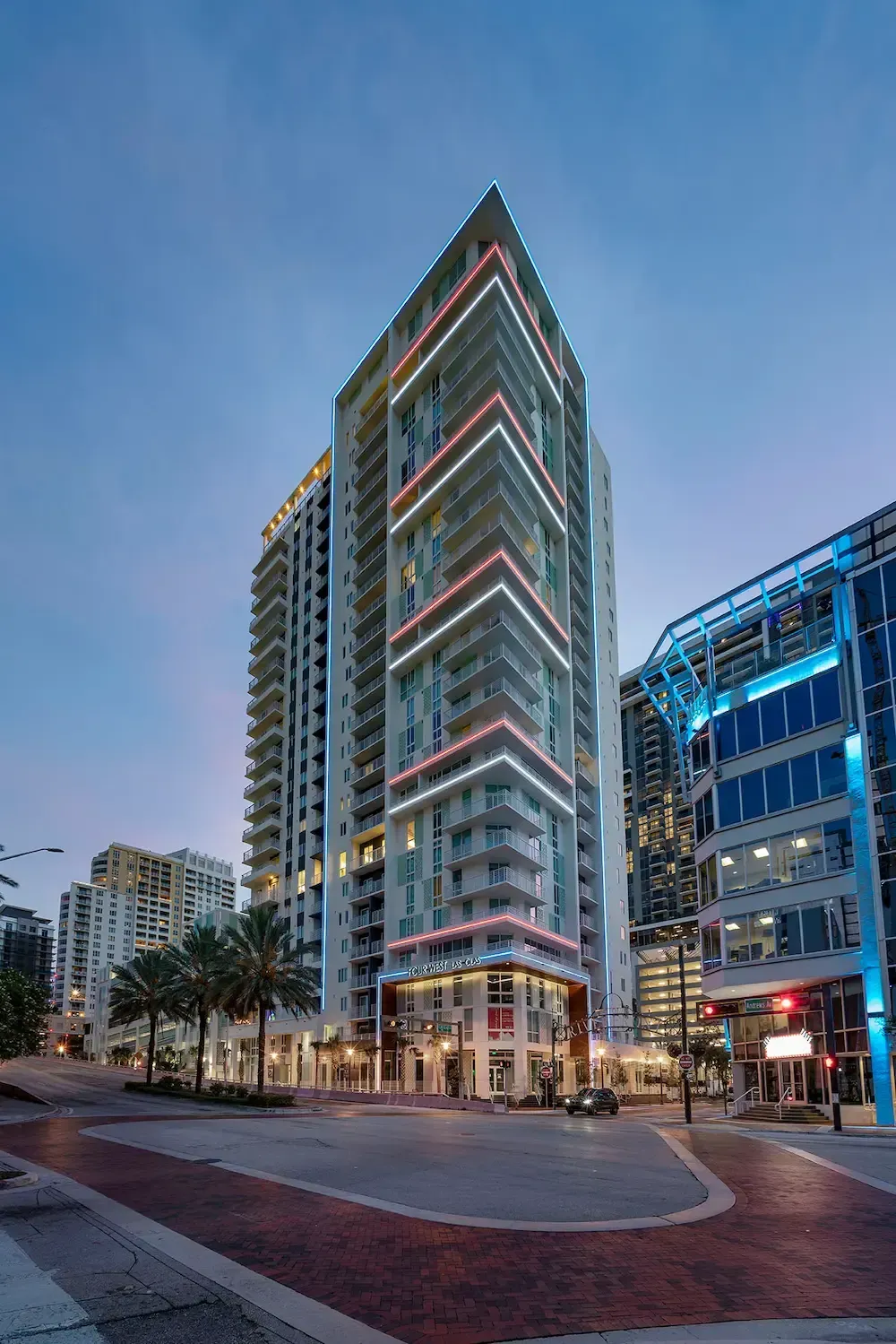 Modern glass high-rise at dusk with lit windows on a city street corner
