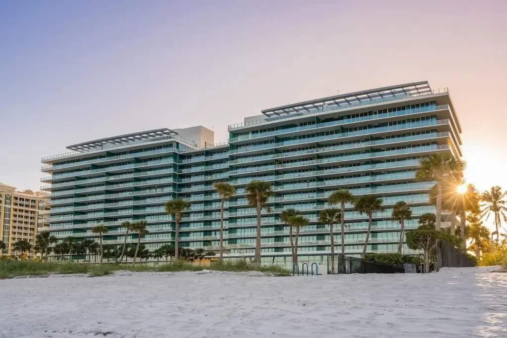 Modern beachfront resort with blue balconies, palm trees, and sunset light on a sandy shore