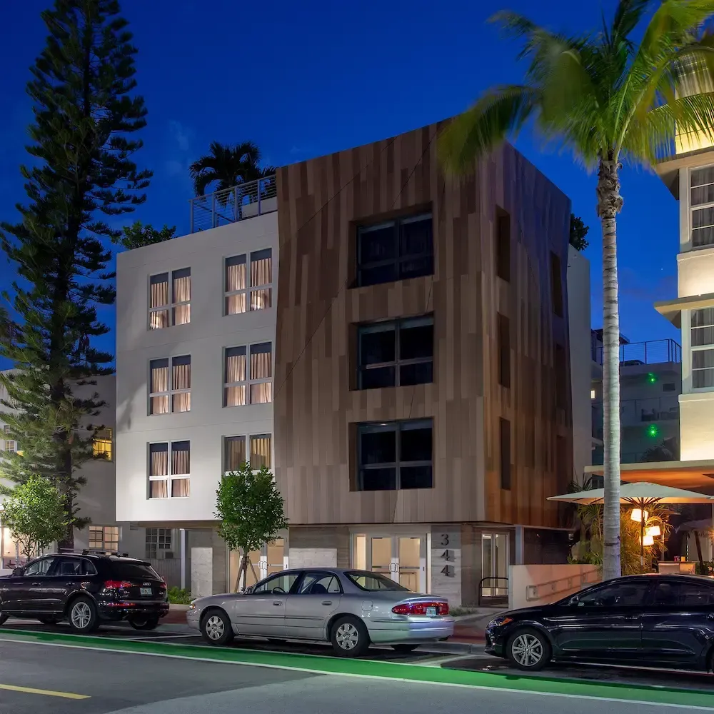 Modern apartment building at dusk with parked cars and palm trees along the street