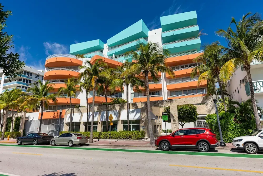 Colorful modern apartment building with palm trees and parked cars on a sunny street