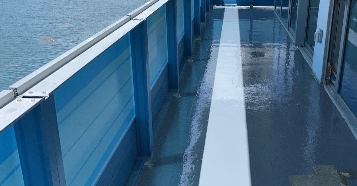 Blue-painted walkway on a ship or ferry deck beside the water, with a wet floor and white center line