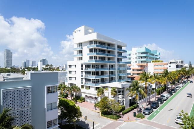 Modern beachfront city street with white apartment buildings, palm trees, and parked cars under a clear sky