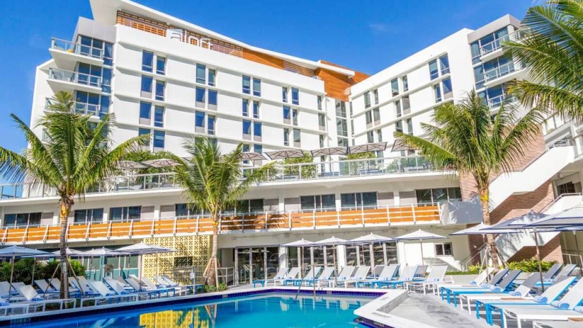 Modern hotel resort with a pool, palm trees, and sun loungers under a bright blue sky