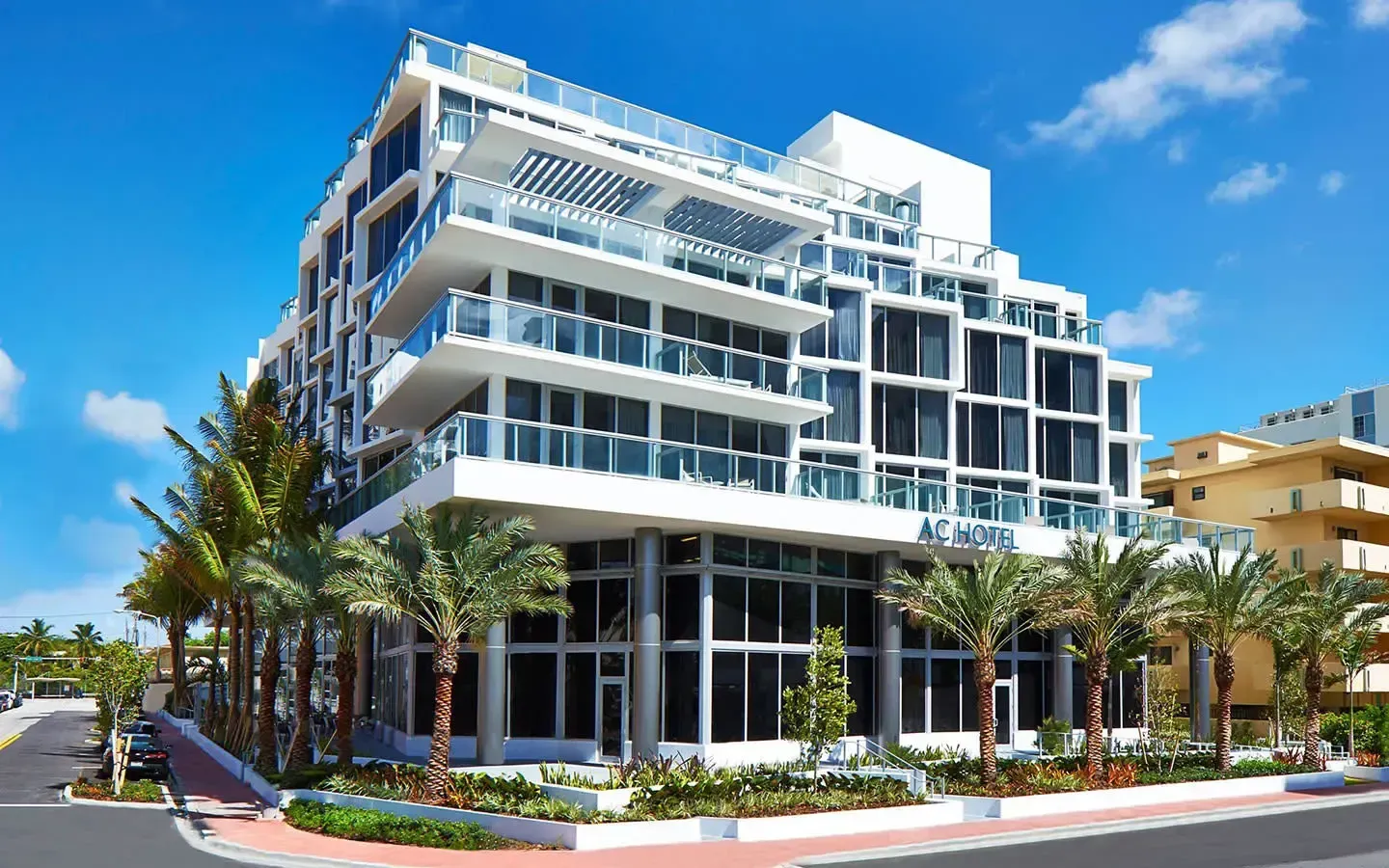 Modern white multi-story apartment building with balconies, palm trees, and clear blue sky