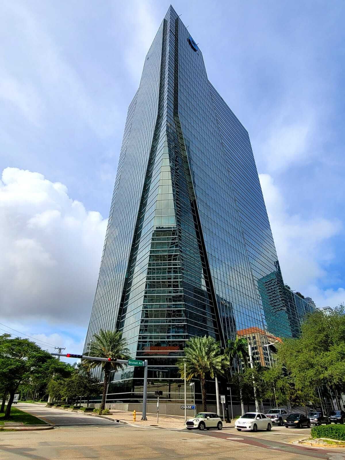 Tall glass skyscraper with a sharp triangular facade beside palm trees under a blue sky