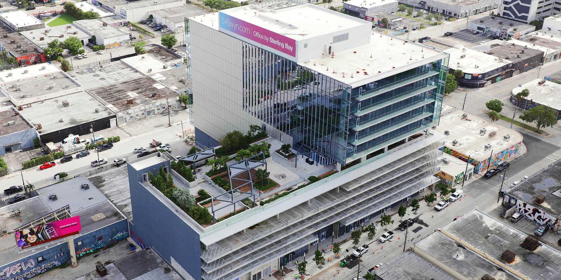 Aerial view of a modern glass office building with rooftop greenery in an urban area