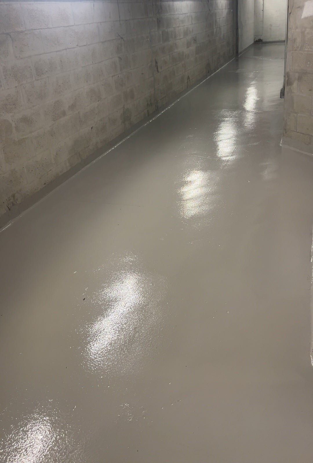Empty concrete hallway with a wet, glossy floor reflecting overhead lights