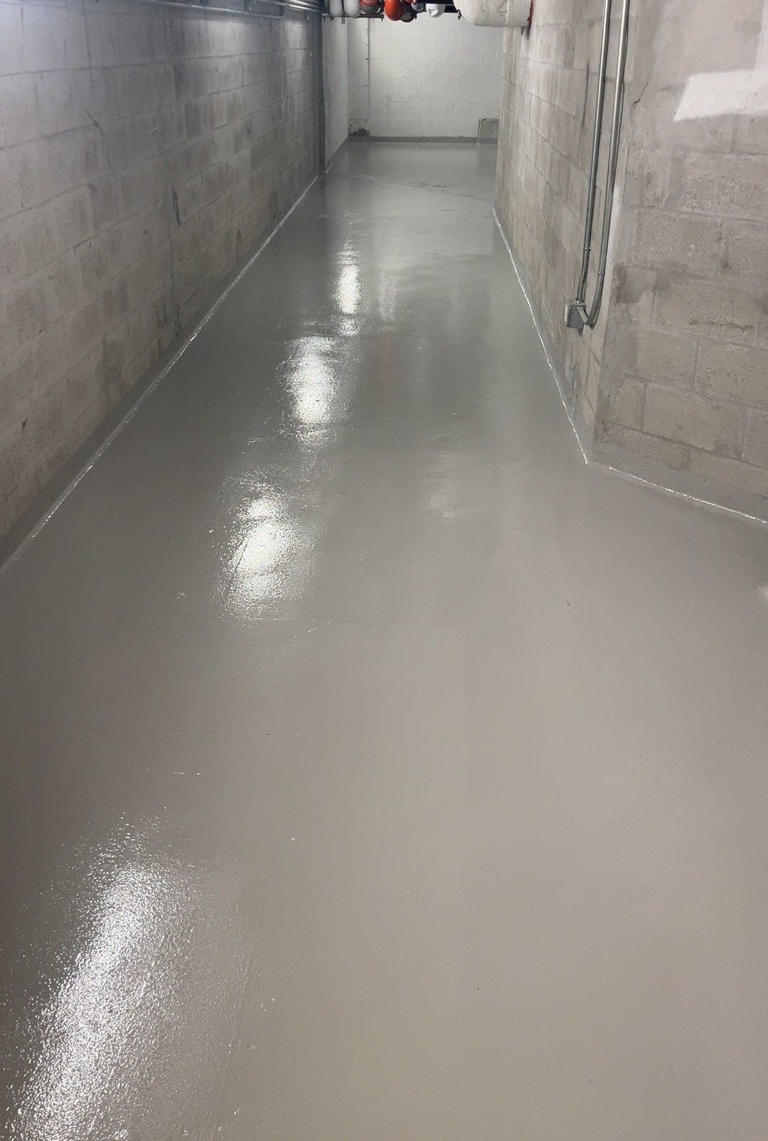 Narrow concrete hallway with wet, glossy floor and gray walls in an unfinished building
