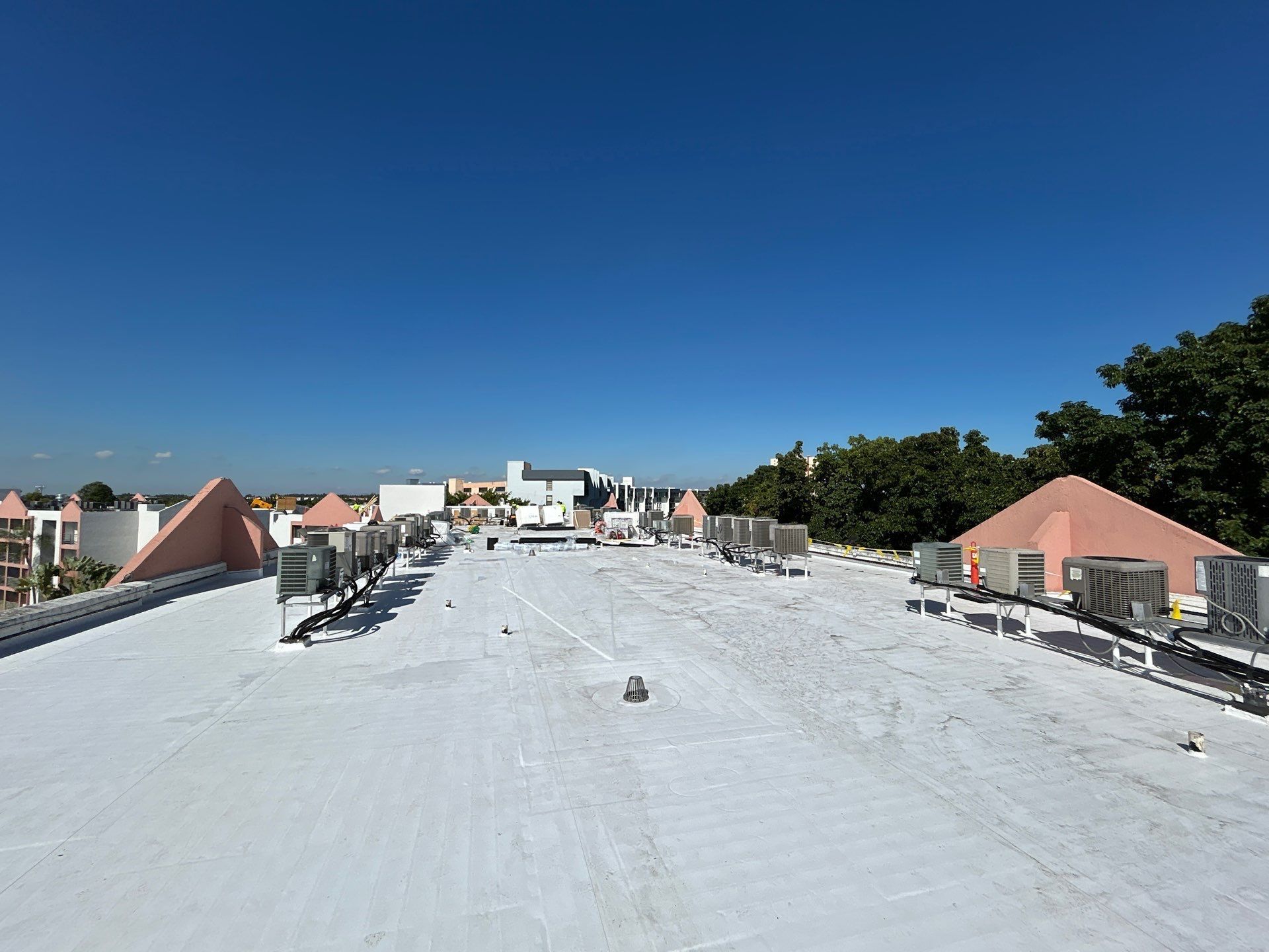 White rooftop under blue sky with HVAC units and low buildings in the distance