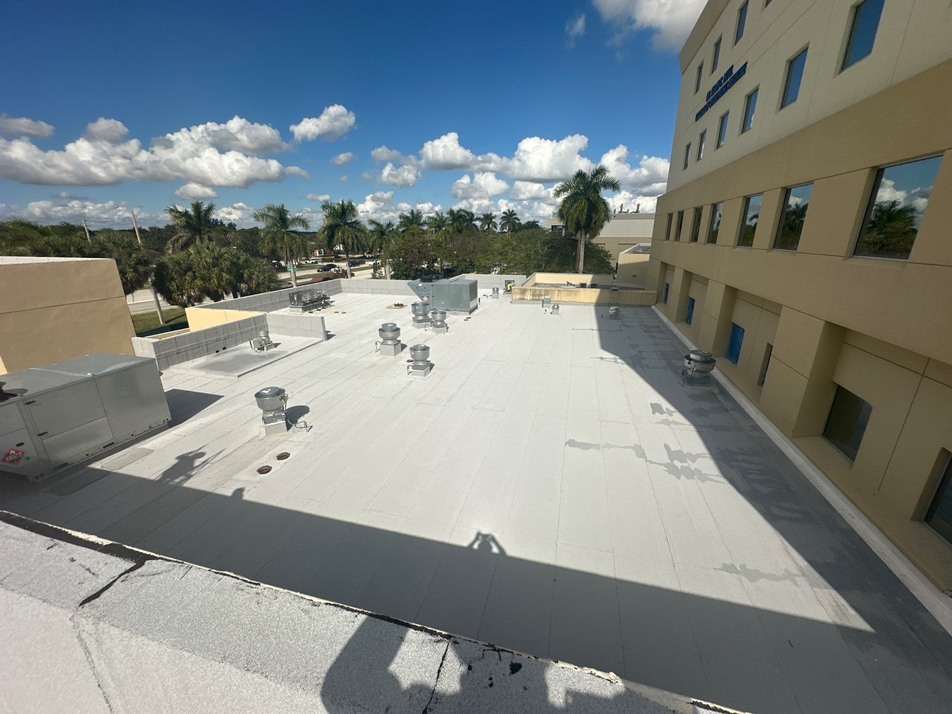 Rooftop terrace with white flooring, chairs, and a beige building under a blue sky with clouds.