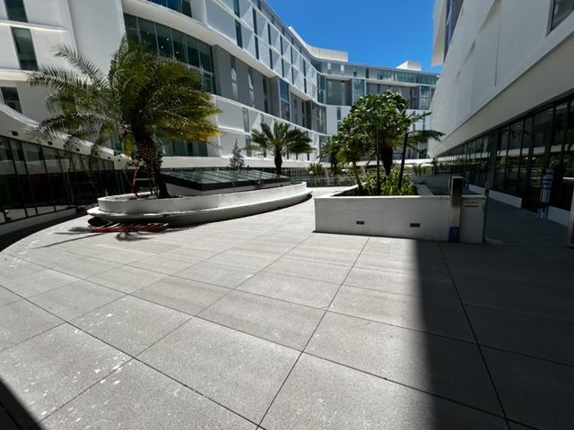 Modern courtyard between white buildings with palm trees and a paved walkway under a blue sky