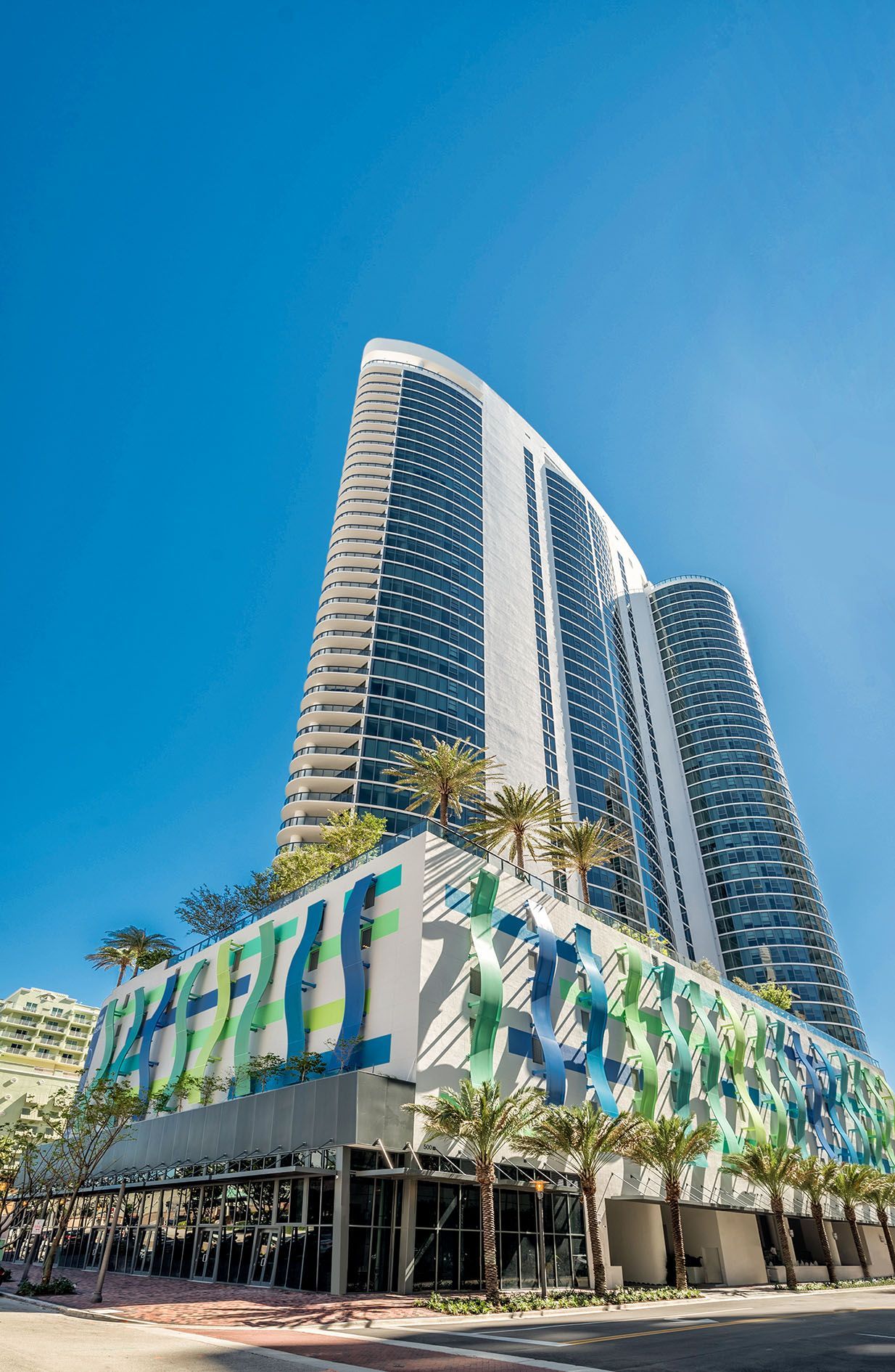 Modern high-rise hotel with curved glass towers and colorful lower facade against a clear blue sky
