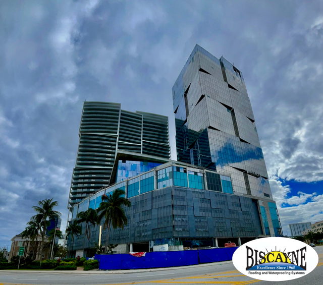 Modern high-rise building under construction with blue glass facade and palm trees against a cloudy sky