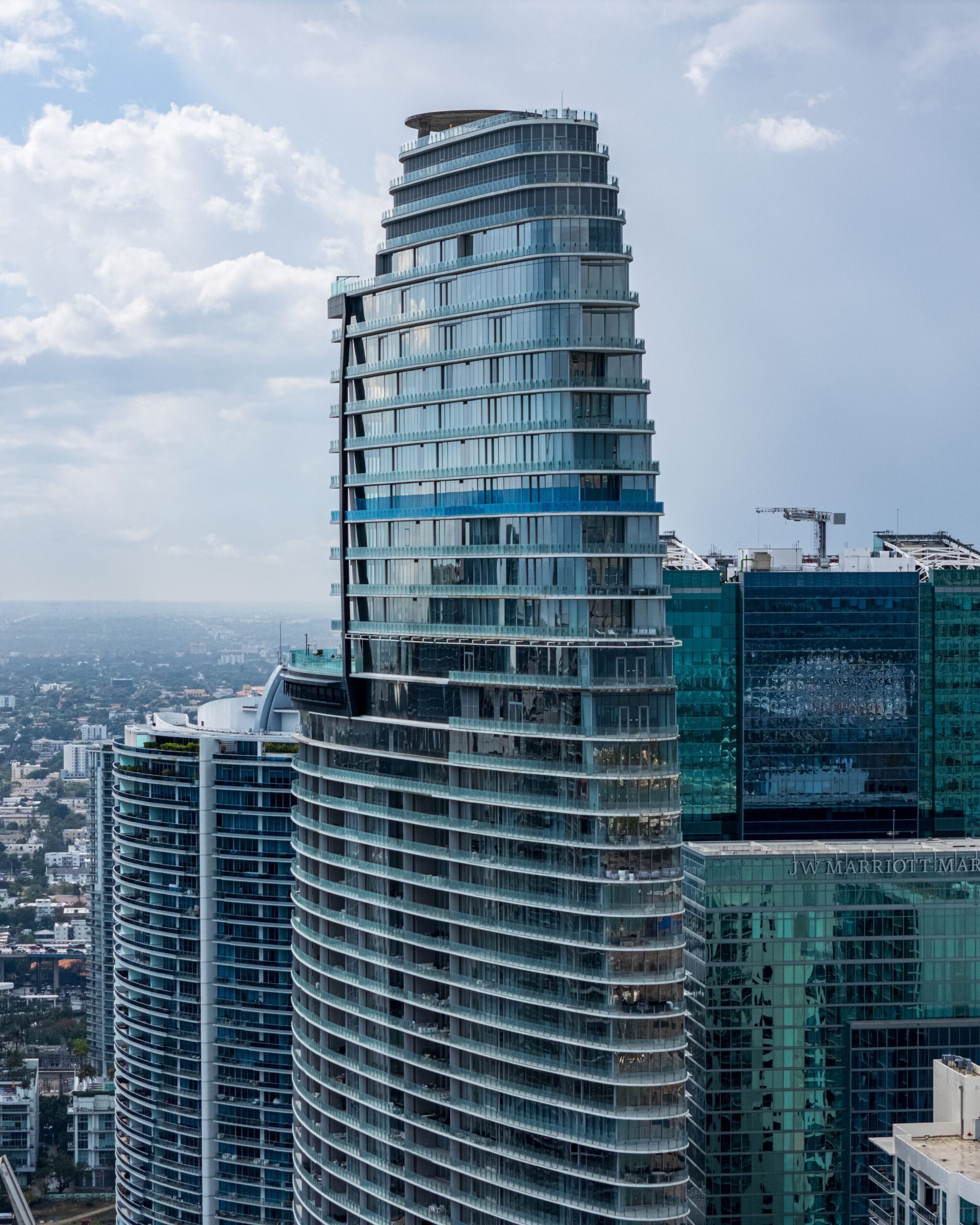 Modern glass high-rise tower rising above a city skyline under a cloudy sky