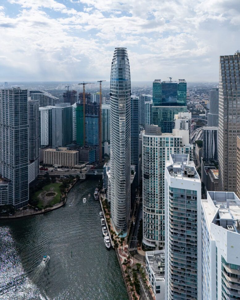 Aerial view of modern skyscrapers lining a river in a dense city skyline under cloudy skies