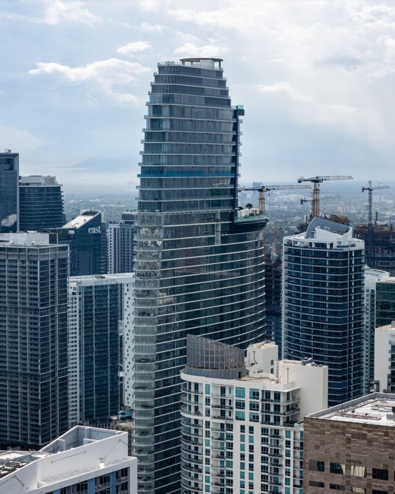 Modern high-rise skyline with a glass tower under construction and cranes in the background