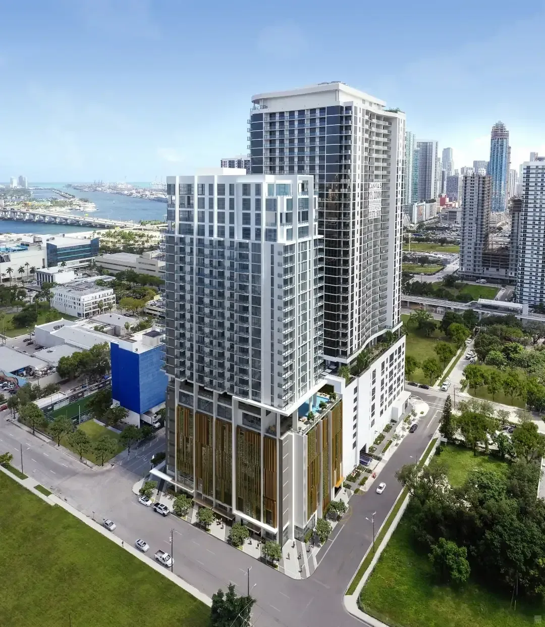 Aerial view of a modern waterfront high-rise building with glass balconies and surrounding city streets.